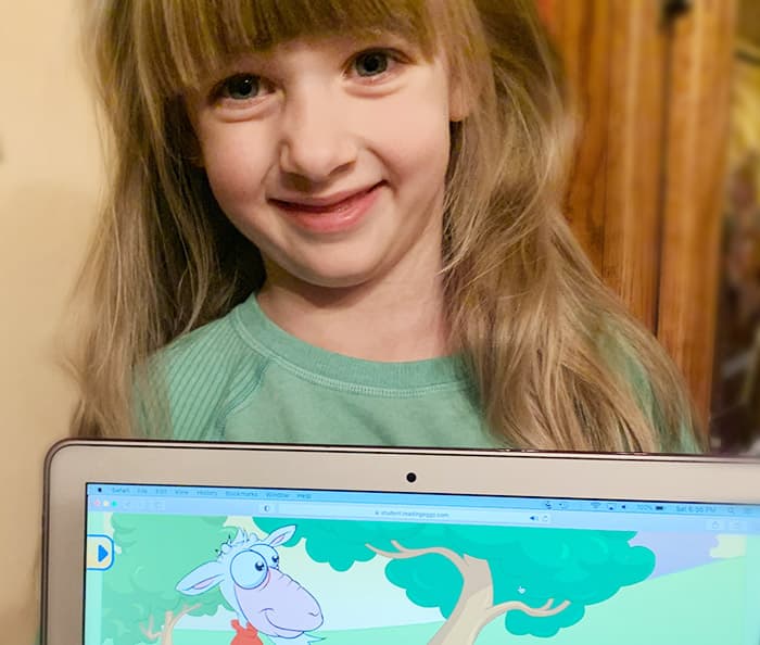 Smiling five year old girl with Reading Eggs online programme on laptop.